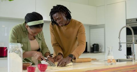 African american couple baking together in bright modern kitchen, cutting dough on island