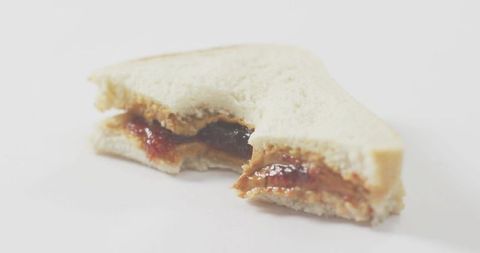 Partially eaten peanut butter and jelly sandwich with bite mark on white tabletop closeup