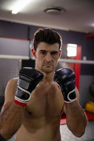 Focused mma boxer raising guard inside cage wearing black gloves and red wrist wraps
