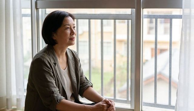 Asian woman sitting by window gazing out over balcony in soft natural daylight