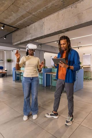 African American duo testing VR headset while partner recording tablet in open-plan office