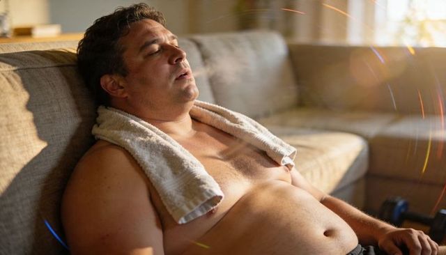 Resting after workout recovering shirtless man with towel reclining on sunlit couch