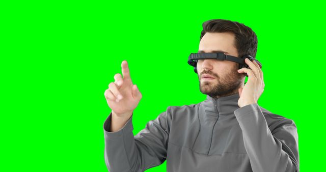 Man using a virtual reality headset while interacting with a futuristic gesture interface against a green screen background. This image can be used for tech blogs, presentations, VR and AR technology advertisements, demonstrations of immersive experiences, and illustrating future innovations in digital interaction.
