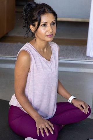 Fit woman sitting cross-legged on mat practicing mindful yoga at home in stylish activewear