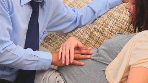 Expecting Couple Relaxing on Sofa with Husband Touching Belly
