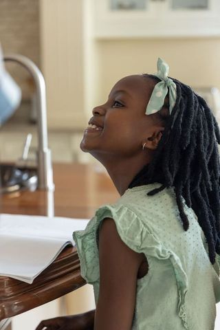 African american girl smiling at kitchen counter wearing mint dress and polka dot headband
