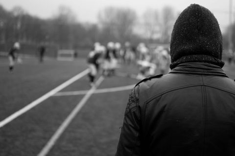 Coach watching youth football game from sideline in cold weather black and white