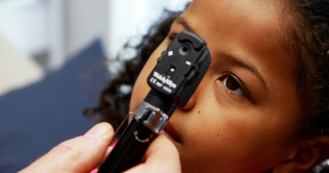Optometrist examining child using ophthalmoscope to check eyesight. The young patient is calm during the examination. Ideal for concepts related to children's healthcare, pediatric optometry, vision screening, health checkups, and medical appointments for children.