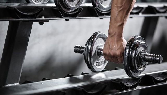 Gripping muscular forearm lifting chrome dumbbell with 20kg plate for strength training
