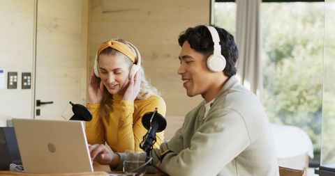 Couple recording podcast in cozy wood cabin wearing headphones and desktop microphones