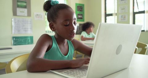 African schoolgirl typing on laptop in bright classroom learning digital skills