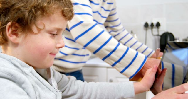 Curly-haired child learning to wash hands with touchscreen guidance in kitchen - Download Free Stock Images Pikwizard.com