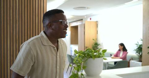 Smiling man leaning at reception counter laughing during coworking lounge conversation