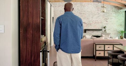 Mature african american man standing in modern farmhouse living room with luggage and denim shirt