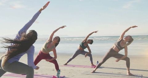 Group yoga session on beach at sunrise, women in athleisure