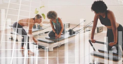 Trainer guiding clients adjusting pilates reformer equipment in bright studio class
