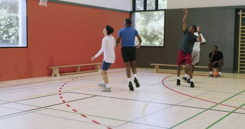 Diverse men playing indoor basketball shooting layup, dribbling crossover, passing, rebounding