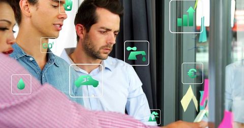 Business team collaborating on sustainable strategy with green icons on glass board