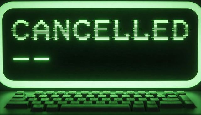 Glowing retro computer monitor displaying cancelled on green pixel terminal with raised keyboard