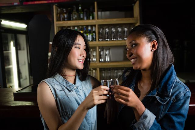 Female friends toasting tequila shot glasses in bar