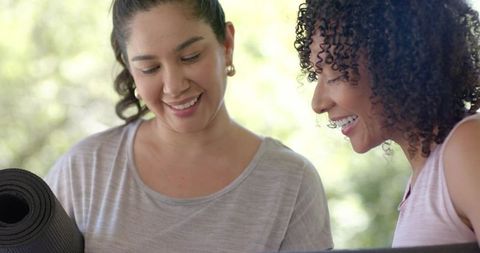 Smiling friends holding rolled yoga mat and checking workout plan together outdoors