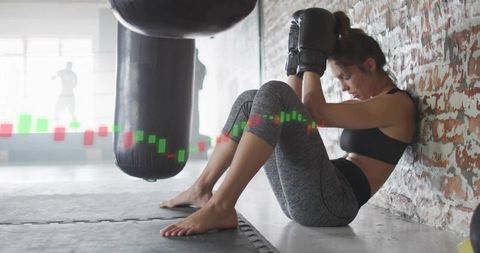 Female boxer resting against brick wall after boxing session with candlestick chart overlay