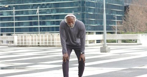 Senior African American Man Catching Breath on Urban Crosswalk Wearing Headphones and Smartwatch