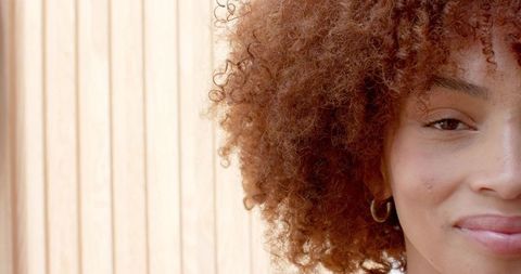 African american woman smiling closeup, curly hair, hoop earring, wooden slat background