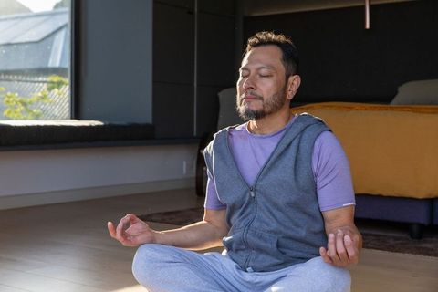 Middle-aged asian man meditating in sunlight wearing hoodie and loungewear for home wellness