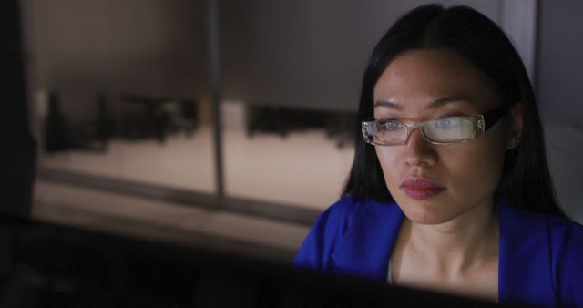 Image of asian businesswoman in glasses staring at computer screen, working at night in office. Business, communication, inclusivity and flexible working concept digitally generated image.