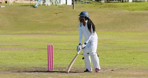 Female Cricket Player Preparing to Bat on Grass Field