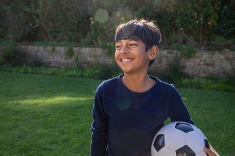 Happy Young Boy Holding Soccer Ball Outdoors in Bright Sunlight