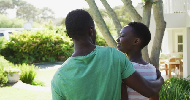 Rear view of smiling african american couple embracing in sunny garden. staying at home in isolation during quarantine lockdown.