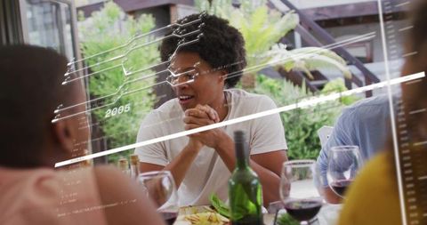 Young man talking and laughing at alfresco dinner with wine and digital hud overlay