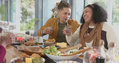 Diverse friends laughing and clinking glasses during cozy daylight brunch and communal meal