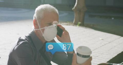 Mature man wearing n95 mask talking on smartphone holding to-go coffee with notifications