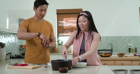 Couple cooking together seasoning and stirring pot on island in modern minimalist kitchen