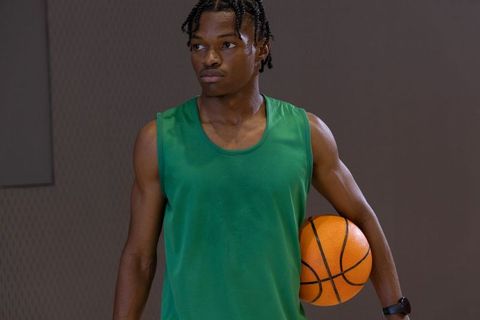 Focused african american teen basketball player wearing green jersey holding ball in gym