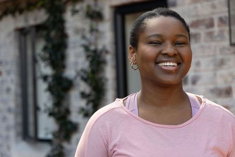 Smiling young woman wearing pink top and gold hoop earrings outdoors by brick facade