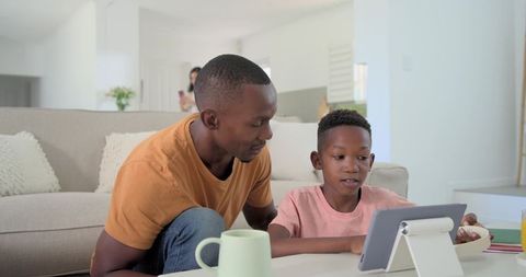 Father and son learning together on tablet in modern bright living room