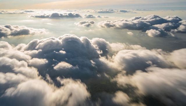 Glowing cumulus cloudscape floating above patchwork landscape at golden hour, aerial view