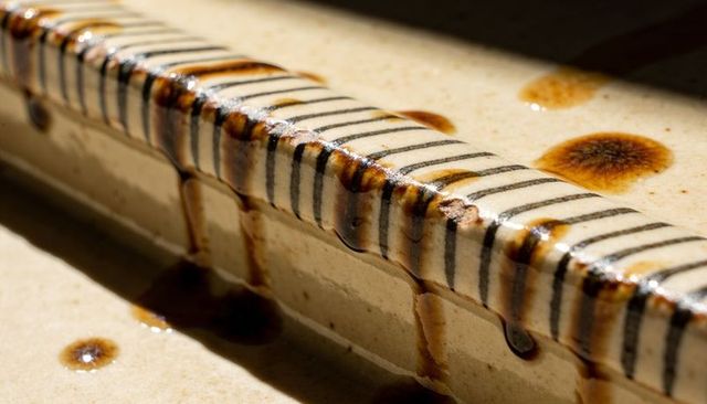 Glazed ceramic tile edge with dripping brown glaze and striped rim, macro texture detail