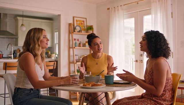 Three friends chatting over brunch at sunlit kitchen table, cozy modern home gathering