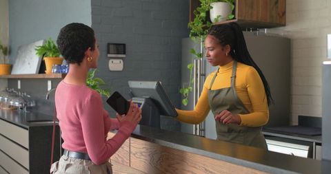 Completing contactless cafe payment at modern wood counter with barista assistance