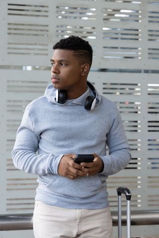 Young african american traveler standing with headphones and smartphone at transit station