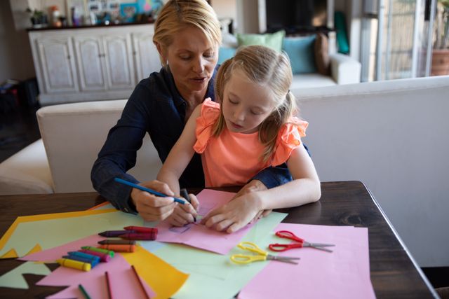Caucasian woman spending family time together with her daughter at home, sitting at table in dining room drawing with crayons creative art. Family leisure time at home.