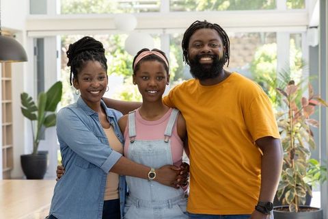 Smiling african family embracing teenage daughter in sunlit modern open-plan home