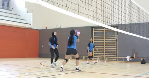 Diverse women's volleyball team practicing indoors playing volleyball wearing hijab and knee pads
