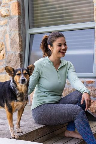Woman relaxing barefoot on porch steps petting tricolor dog in casual athleisure moment