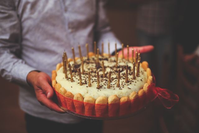 Man holding decorative birthday cake with multiple candles suggests a celebratory occasion. This can be used to depict moments of joy, parties, and festive gatherings. Perfect for use in articles about birthdays, party planning, and celebratory events.